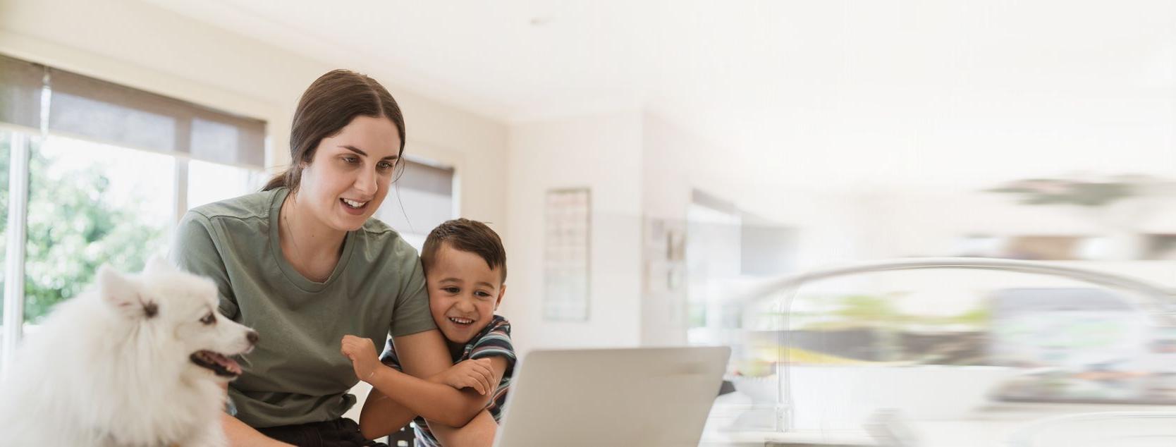 A mother, preschool boy and small dog on a video call with a laptop.